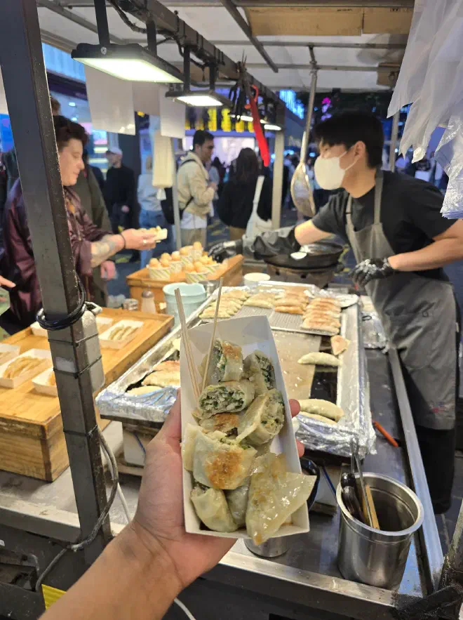A box of dumplings being held with the stall where a man sells dumpling in the background