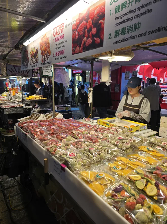 A woman stands a stall selling various colourful dried fruit wrapped in plastic