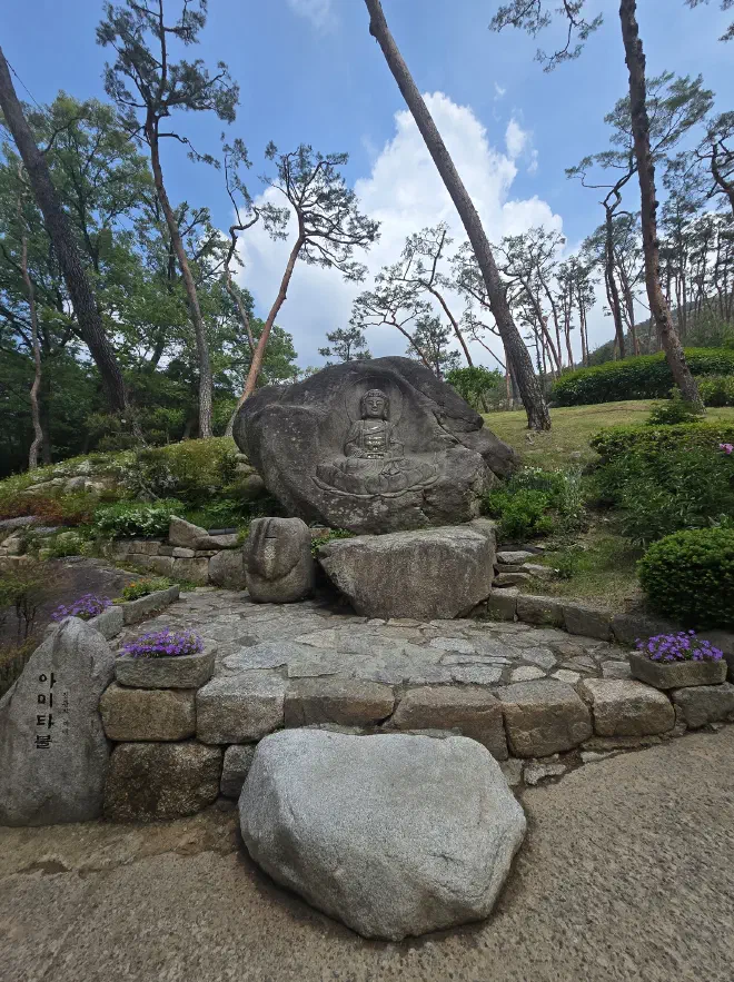 Stone steps leading up to a likeness of the Buddha carved into a rock with a small donation box to its left