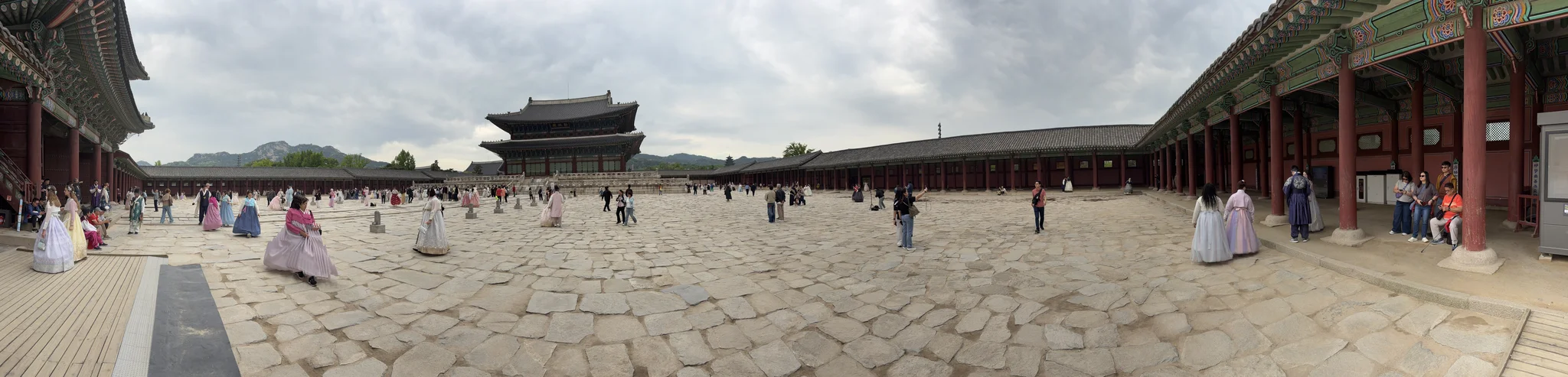 Many people wearing traditional Korean clothing standing in a stone courtyard surrounded on all sides by traditional Korean buildings