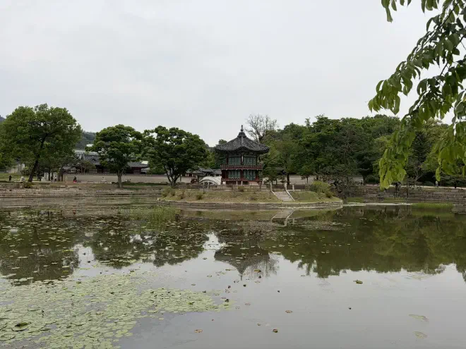 A traditional multi-storey Korean building sits in the middle of a lake flanked on both sides by trees
