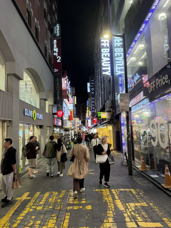A woman in a brown knee-length jacket walking down a busy street at night