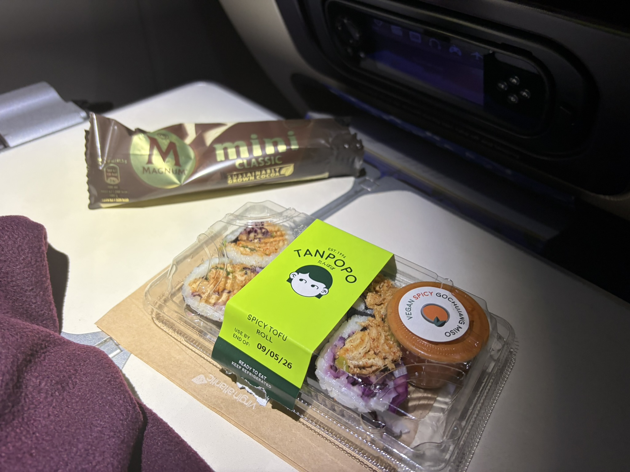 Sushi and an Ice Cream A box of 6 sushi maki with a spicy sauce and a mini Magnum ice cream sit on the tray table in an aeroplane