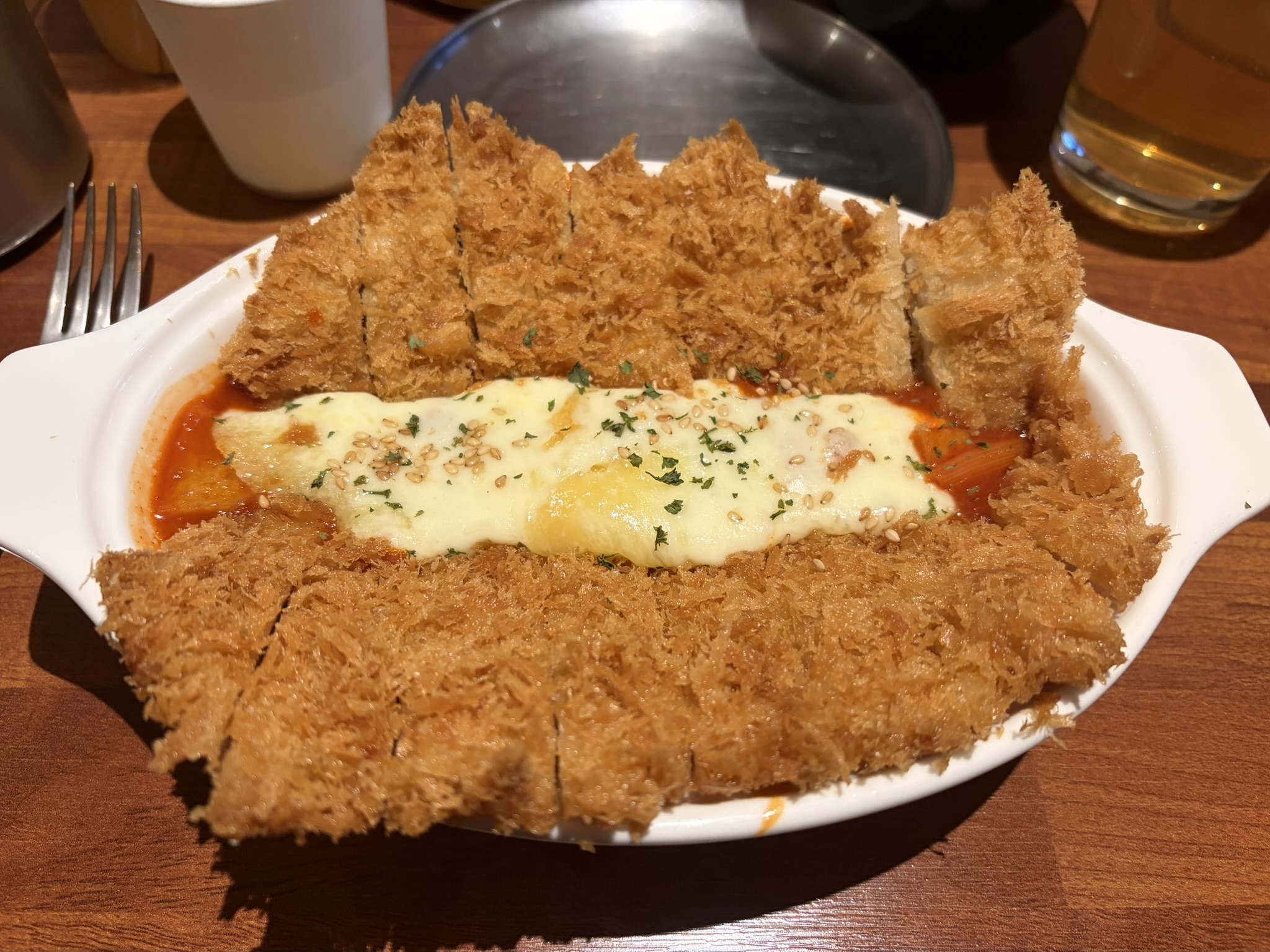 Chicken & Tteokbokki A white dish on a wooden table with breaded chicken cutlets on a spicy red sauce