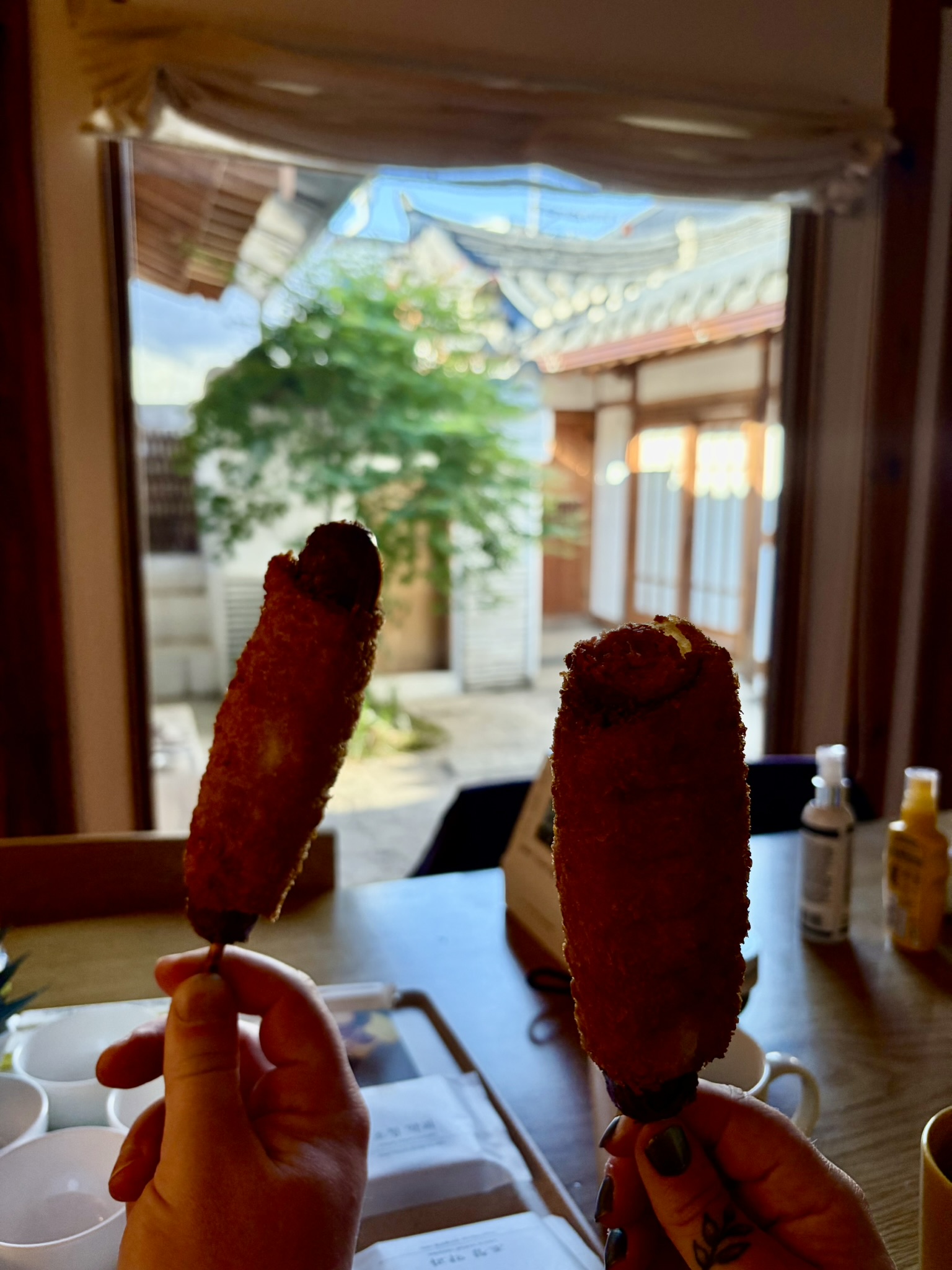 Battered Hot dogs Two people holding up battered hot dogs on sticks. In the background the sun is shining on a courtyard