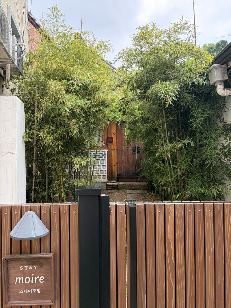 A wooden gate and a sign saying &lsquo;Stay miore&rsquo; and behind it a short path with bamboo either side leads to a wooden door