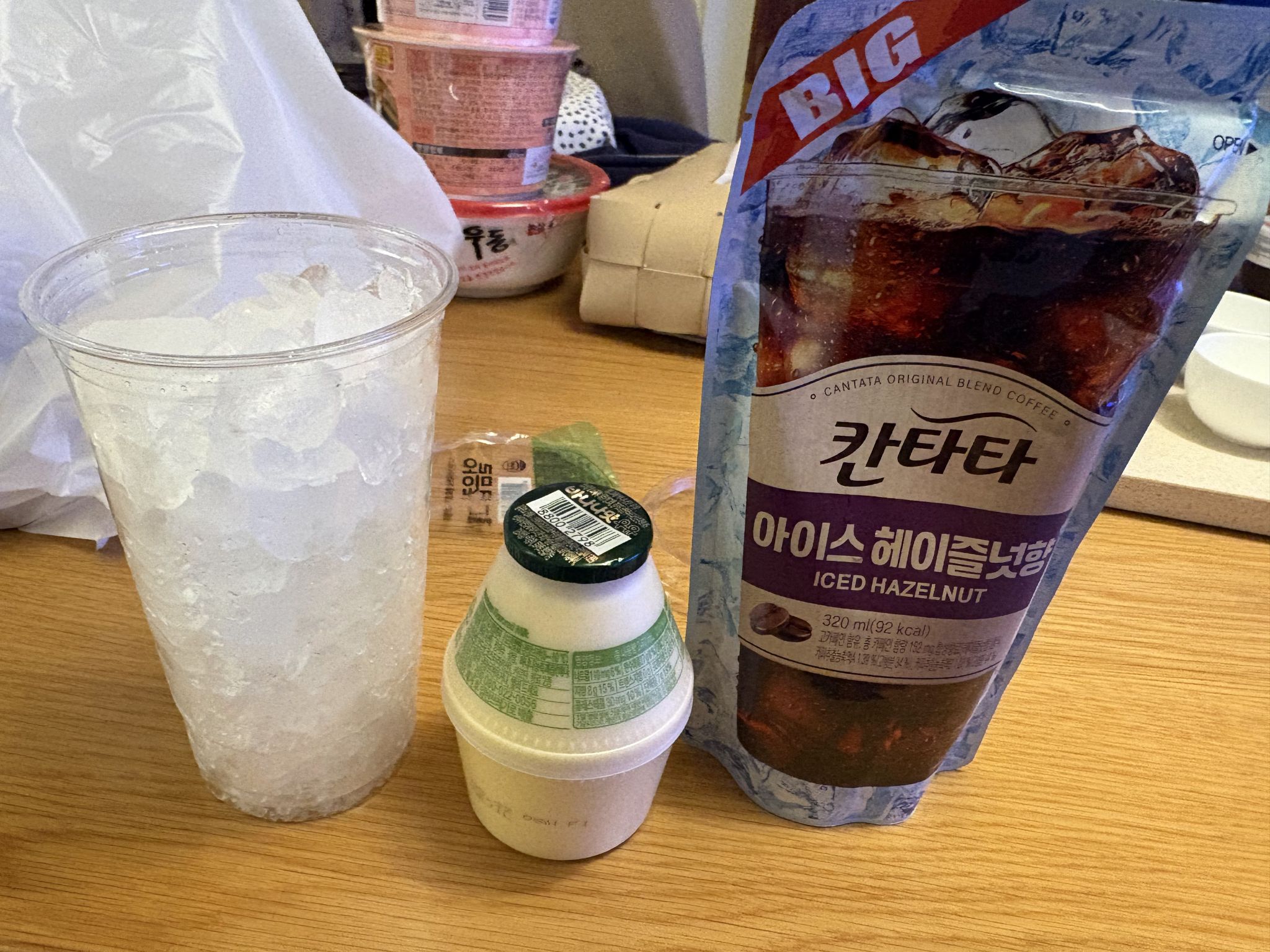A cup of ice, Hazelnut Coffee, and Banana Milk A cup of ice, Hazelnut Coffee, and Banana Milk on a wooden table