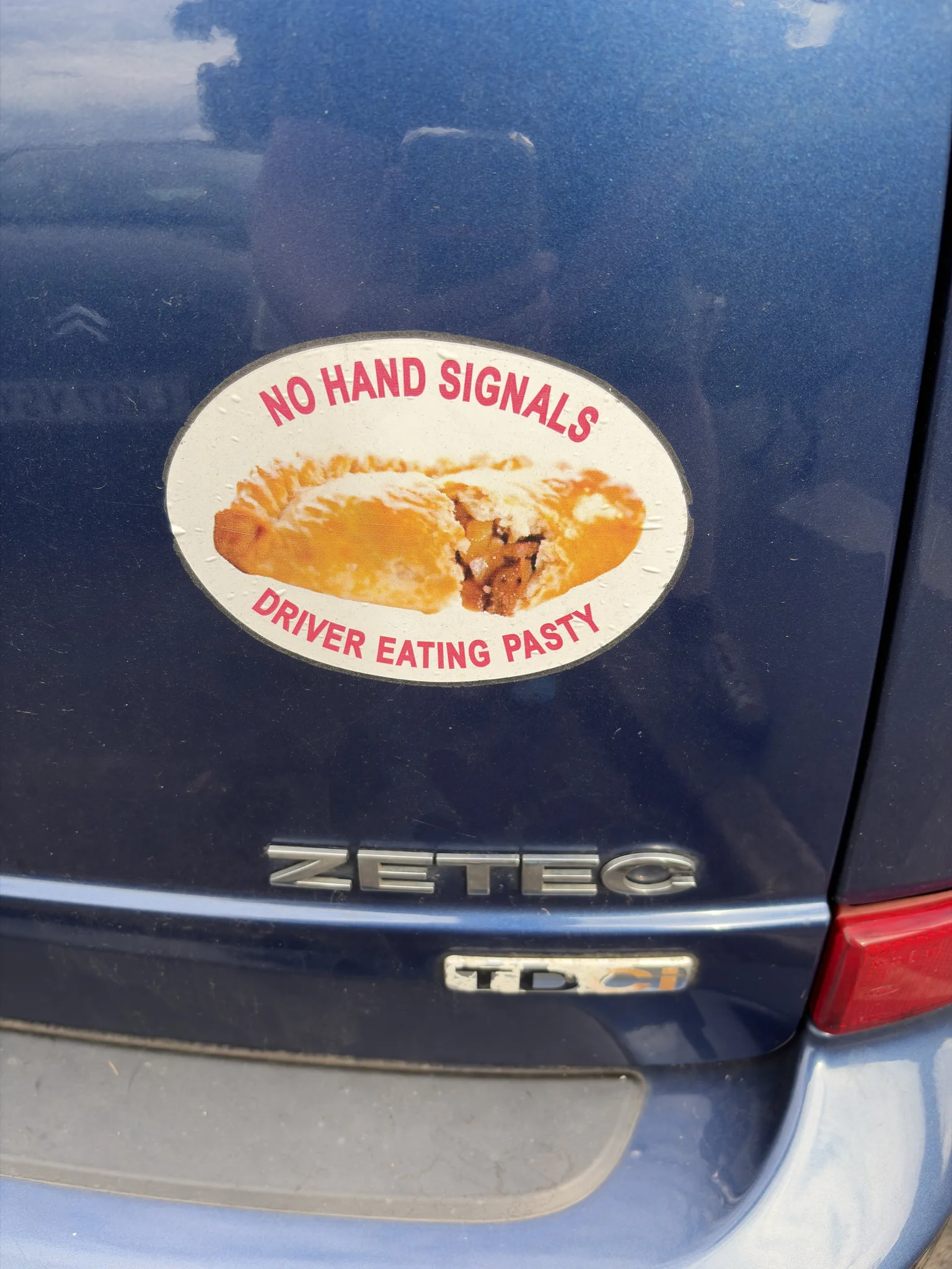 A sticker on a blue car with the words ‘No hand signals, driver eating pasty’ around the picture of a Cornish Pasty