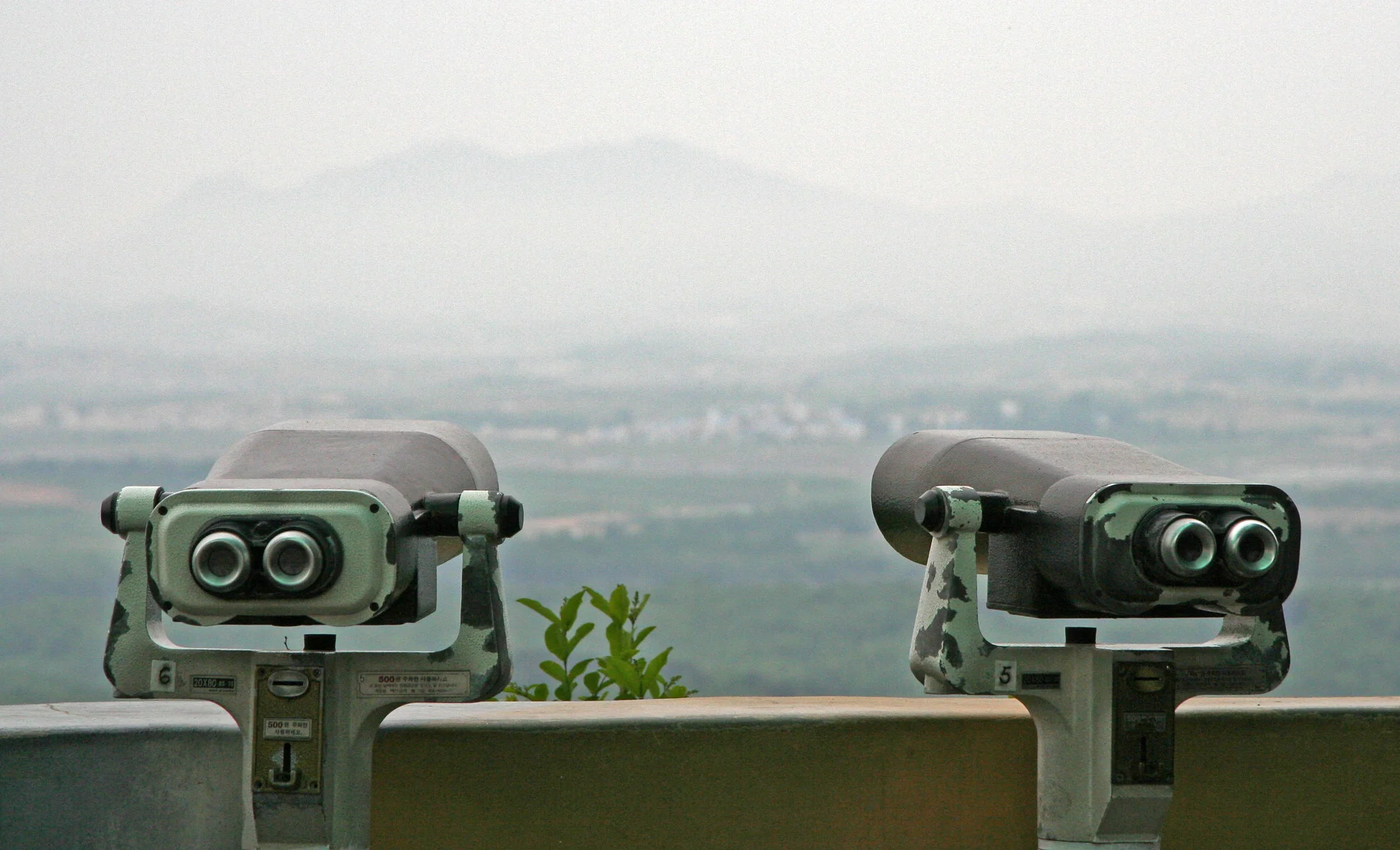 Two pairs of binoculars on poles look out over a misty landscape