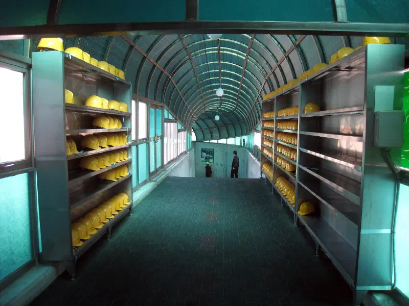 Shelves containing hard-hats line the walls of a corridor that has a steep decline