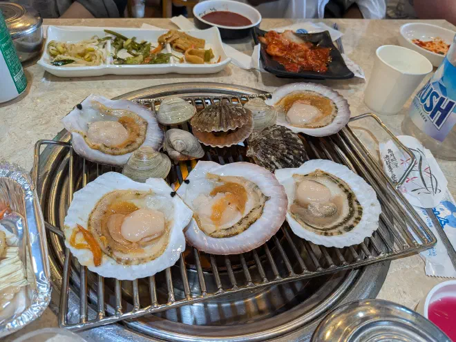 Korean Seafood BBQ Clams being cooked over a grill in the middle of a table covered by plates