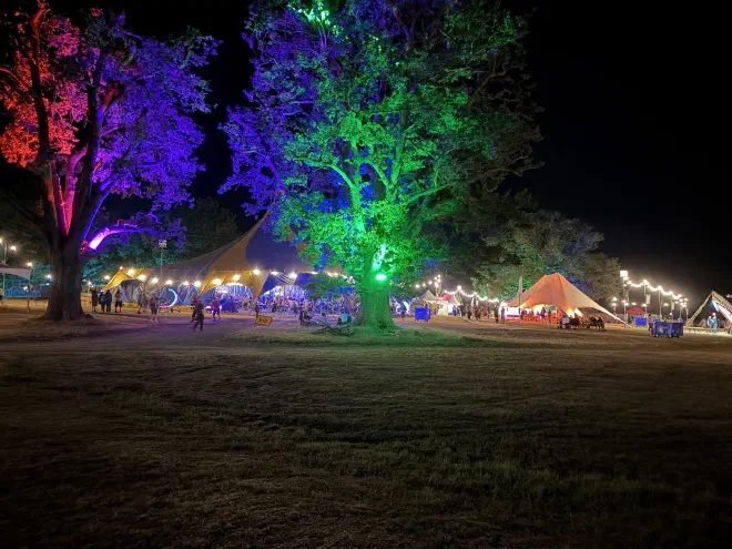 Coloured lights shine on trees at night with multiple marqees in the background