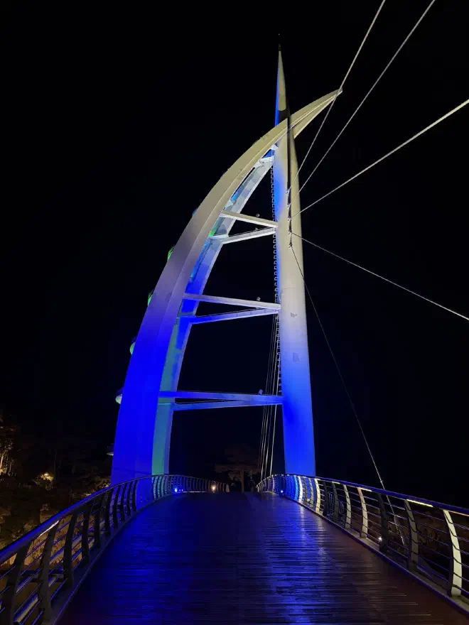 A wooden walkway with an illuminated support lit in blue light at nighttime