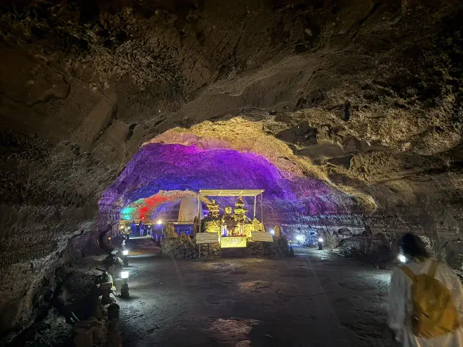 An illuminated cave stretches into the background behind an alter, illuminated with purple and yellow lights