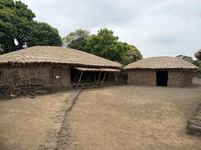 Two stone buildings with thatch roofs positioned around a dirt courtyard