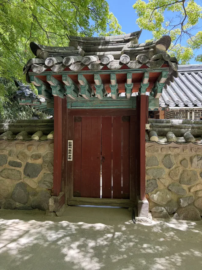 A red door in a five-foot stone wall covered by a tiled awning