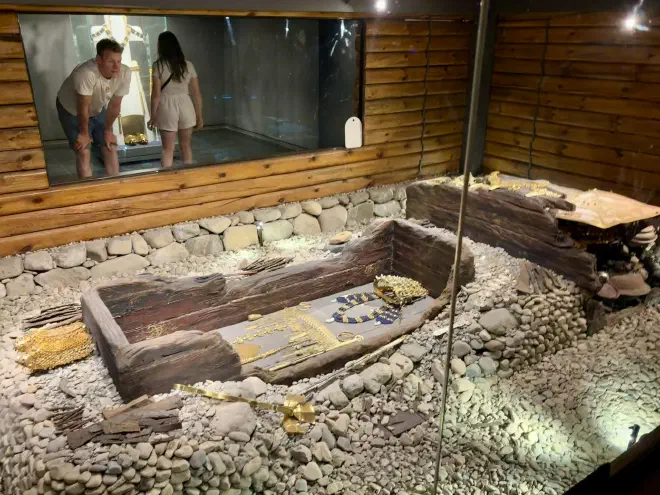 An old wooden coffin with gold regalia inside a glass room