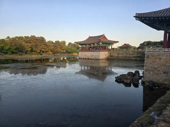 Two red wooden pavillions on stone bases overlook a stagnant pond with trees surrounding it