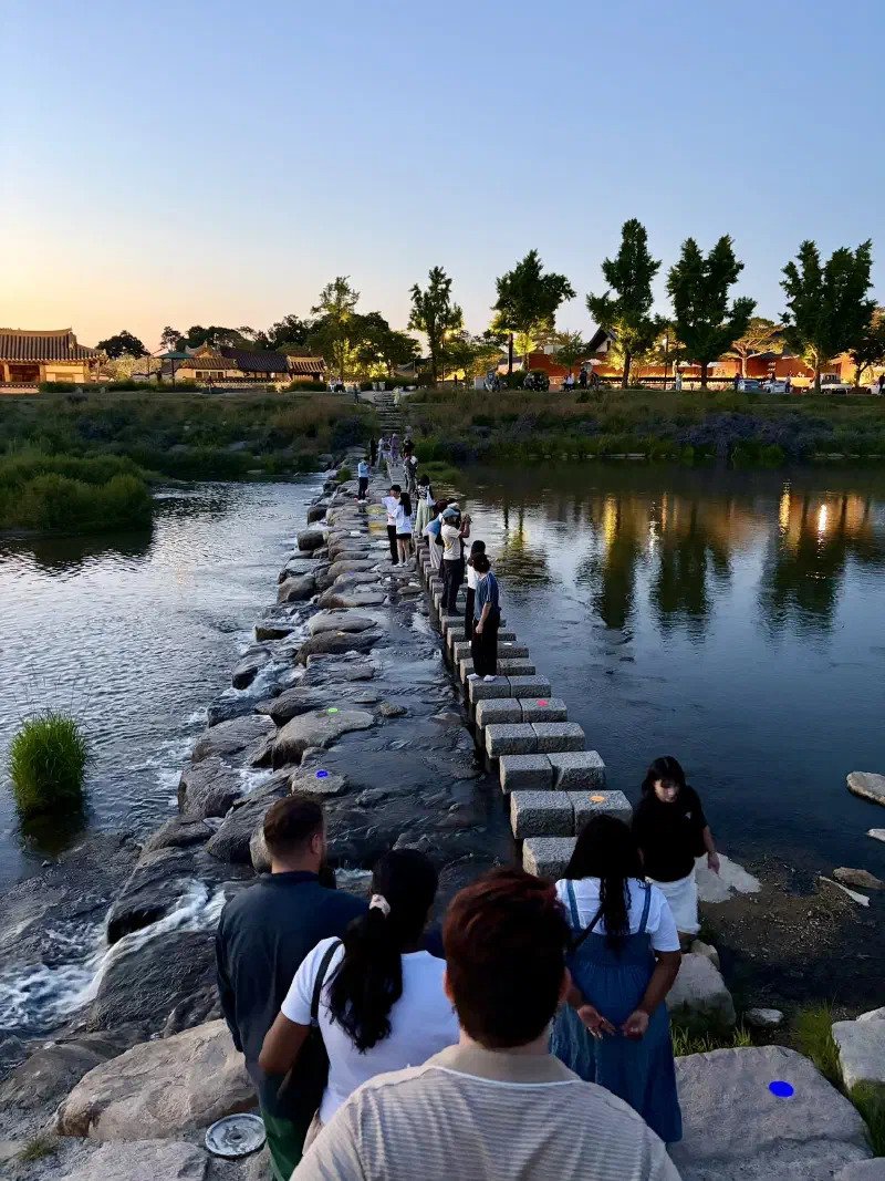 People taking pictures stand on stepping stones over a river