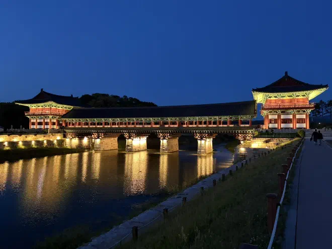 A traditional wooden bridge at night with lights illuminating the underside of the structure