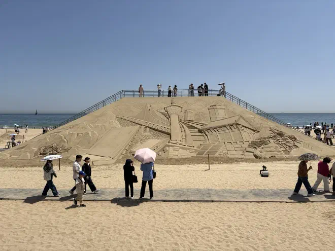 A sand sculpture with images depicting landmarks around Busan with a walkway over the top