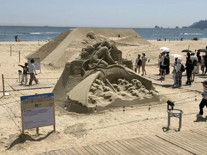 A sand sculpture with a representation of a character from Avatar: The Way of Water with the ocean in the background