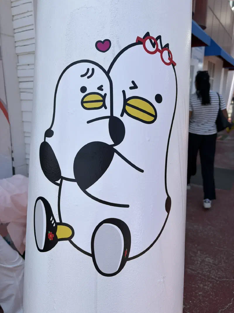 A lamppost with a sticker of a seagull with glasses holding a younger seagull
