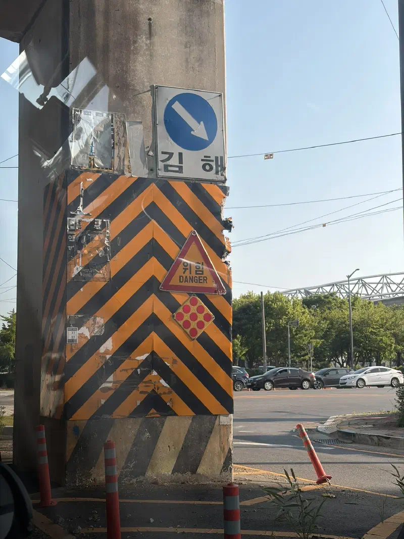 A giant concrete pillar wrapped in a giant orange chevron, with a reflective diamond, and a danger sign, with multiple chunks taken out of it