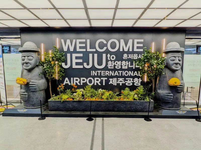 A welcome to Jeju sign with stone statues either side of it