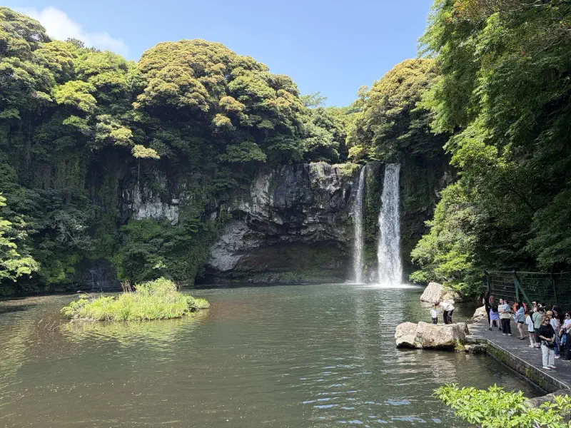 A lake surrounded by cliffs with a waterfall to one side while people look on
