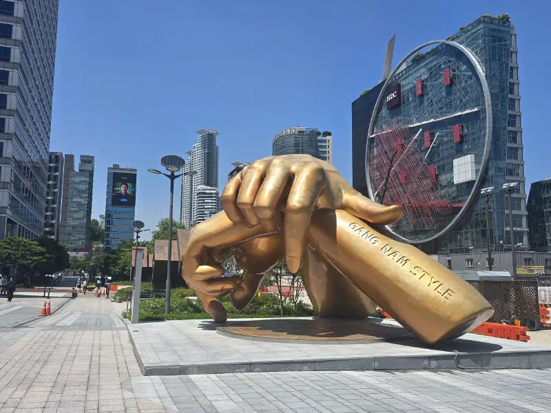 A statue of giant golden hands sits between tall glass buildings