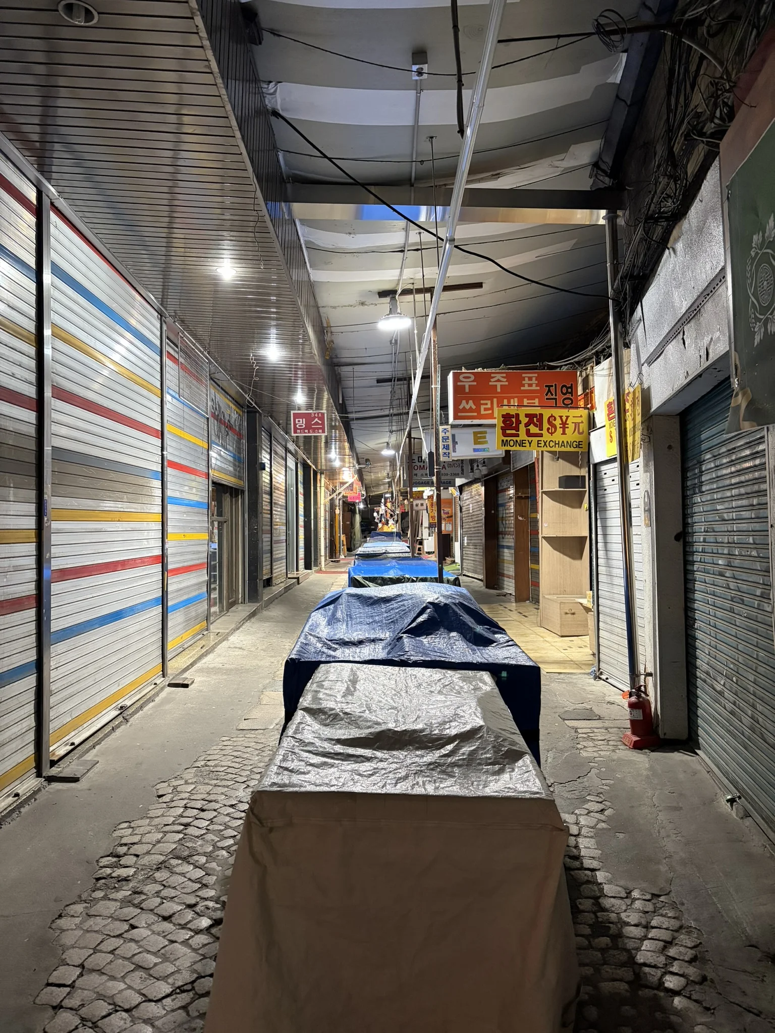 A quiet street in Seoul A long street with shuttered shops and a row of covered tables down its centre