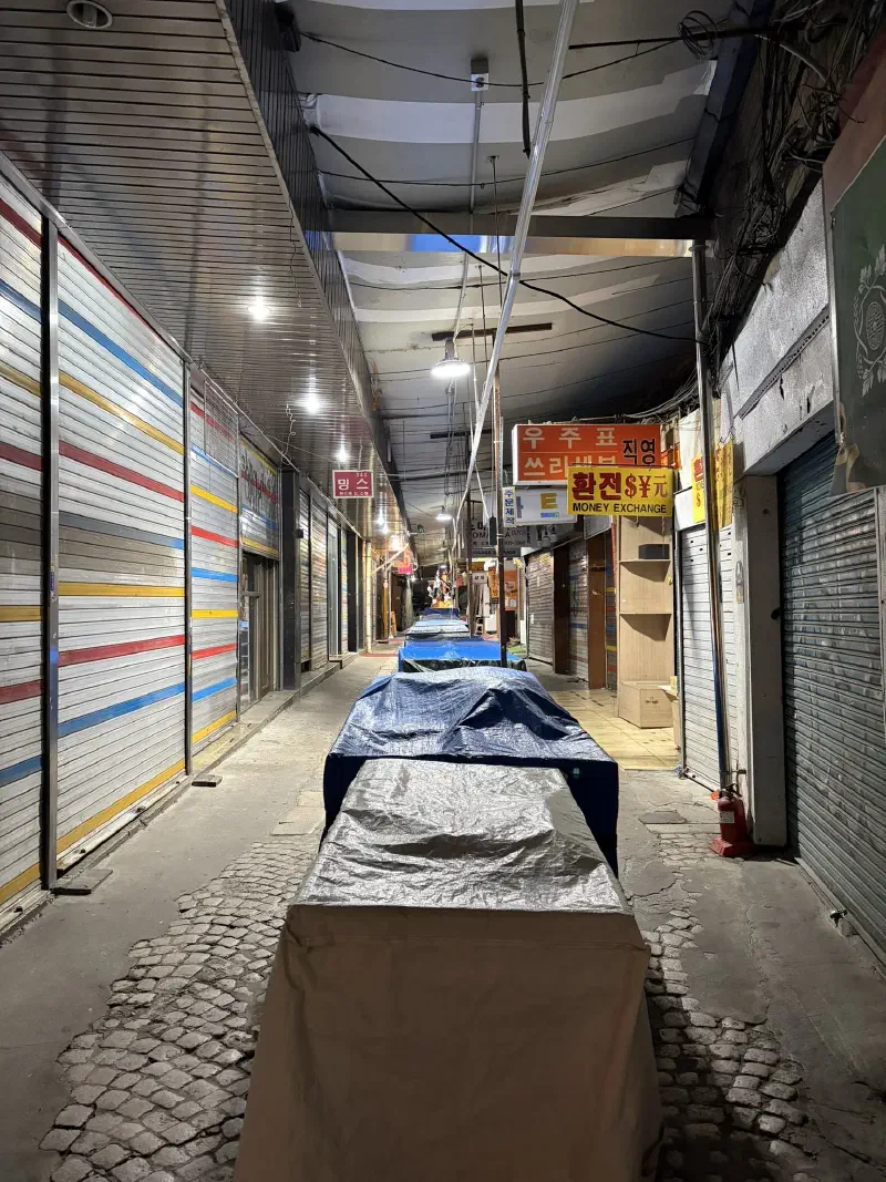 A long street with shuttered shops and a row of covered tables down its centre