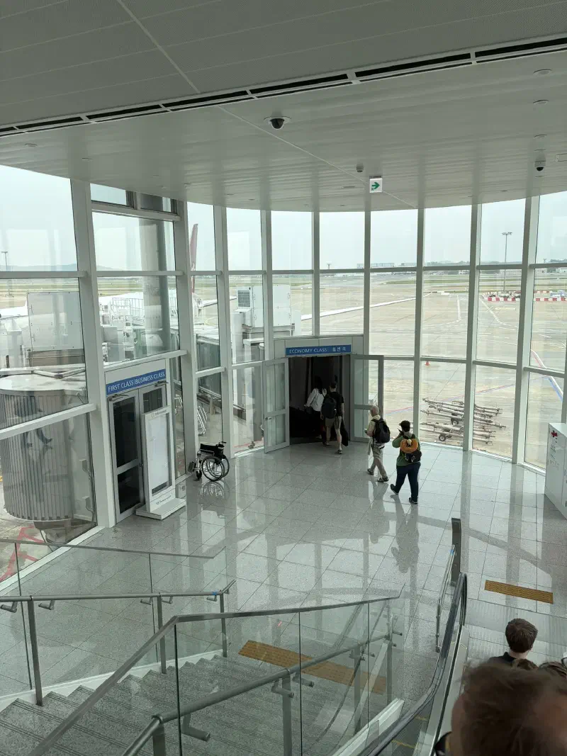 A tall windowed room with people exiting towards a plane