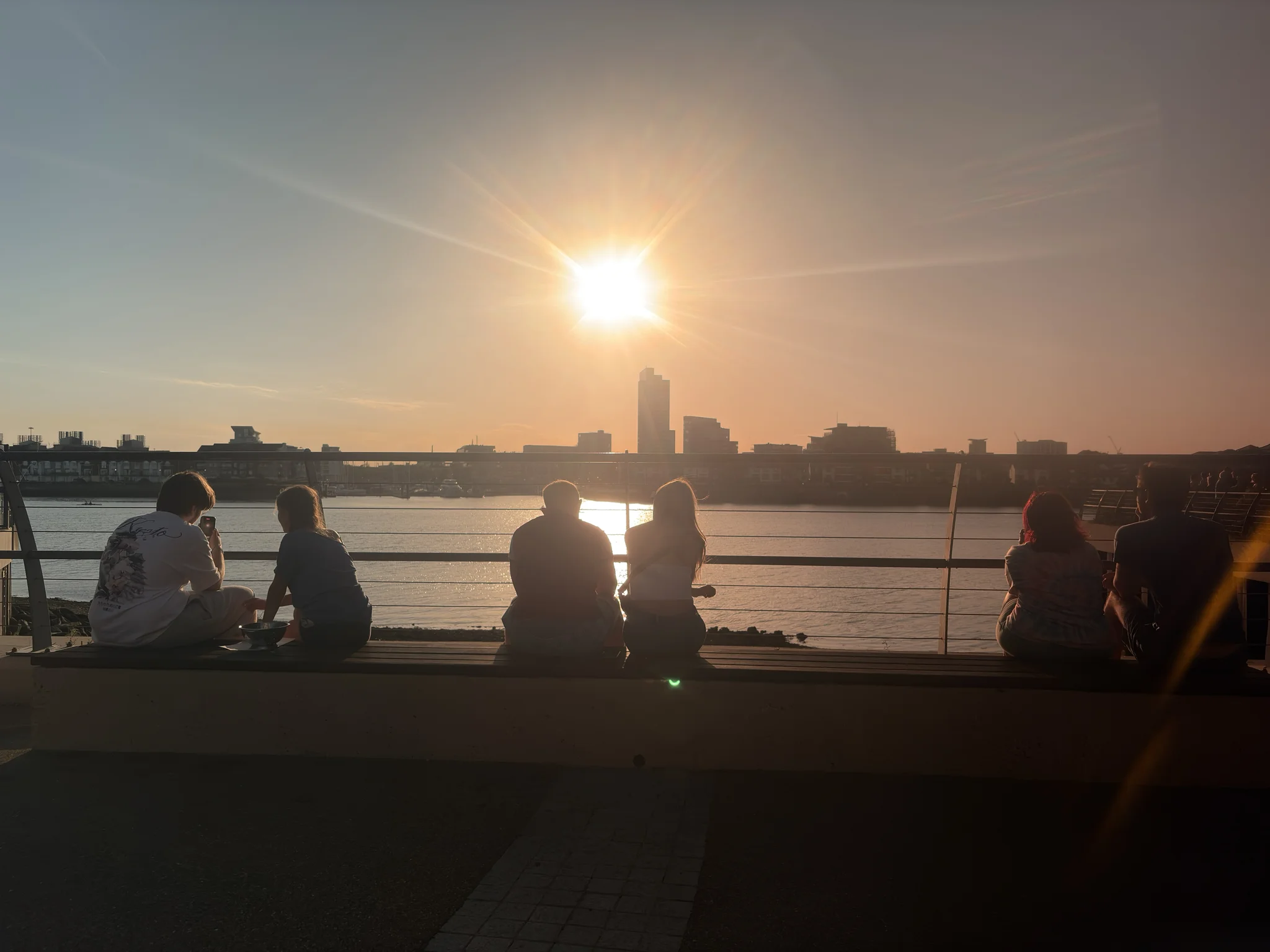 A beautiful spot to watch the sun disappear People sitting on a bench looking out over water towards a dimming sun